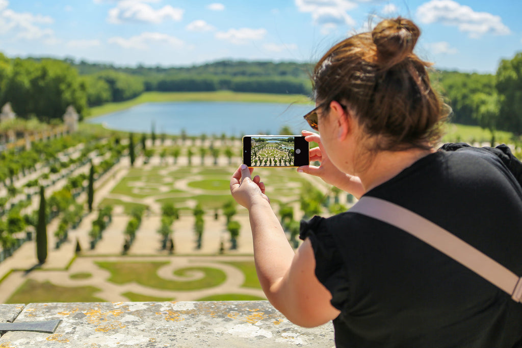 Palace of Versailles, Gardens. Woman enjoying audio Guided Tour via smartphone from Paris